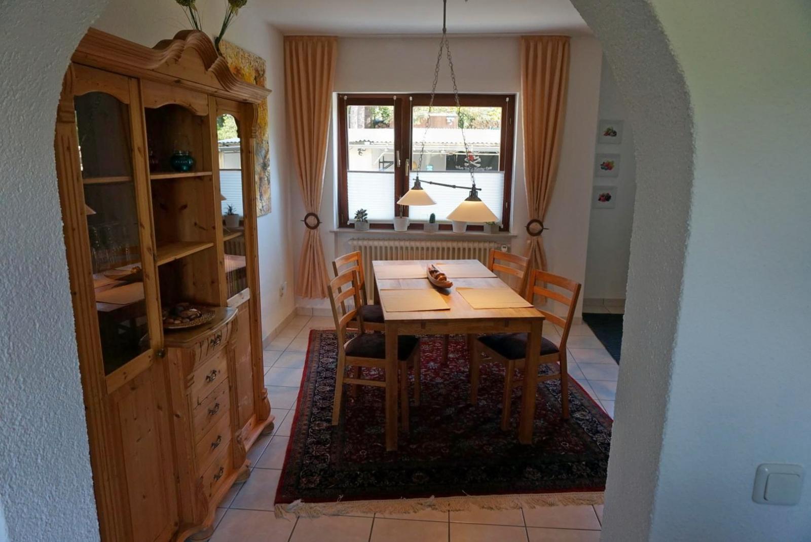 Esszimmer mit Esstisch am Fenster und Holzvitrine, durch den Torbogen gesehen